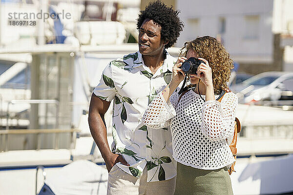 Mann steht mit Freundin und fotografiert am Hafen