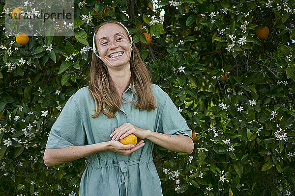 Glückliche junge Frau steht vor einem Orangenbaum im Obstgarten