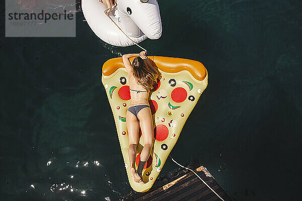 Frau schwimmt auf einer Pizza-Luftmatratze im Meer