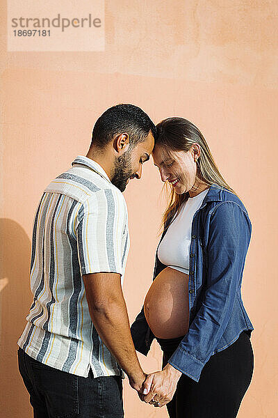 Mann hält Händchen und steht mit schwangerer Frau vor der Wand