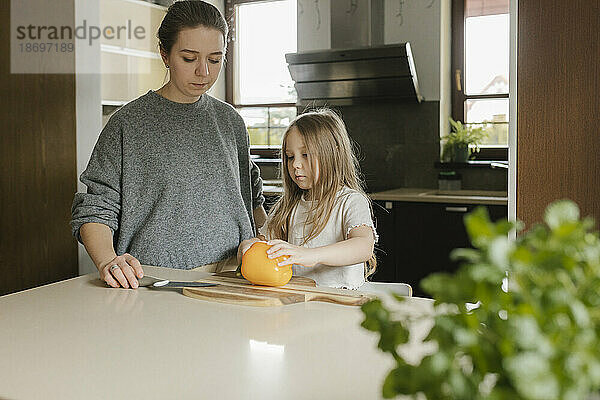 Tochter lernt von Mutter zu Hause  gelbe Paprika zu schneiden