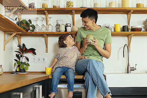 Glückliche Frau sitzt mit Sohn zu Hause auf der Küchentheke
