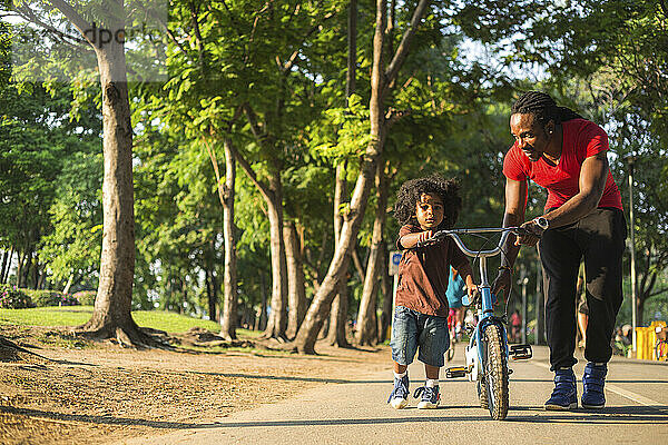 Vater fährt mit Sohn Fahrrad auf Fußweg im Park