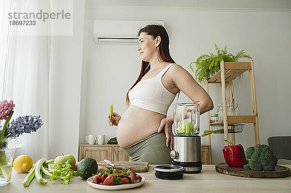 Schwangere Frau mit der Hand auf der Hüfte steht zu Hause in der Küche