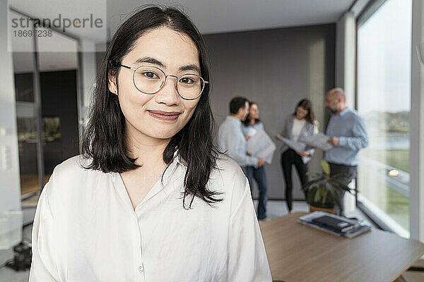 Porträt einer selbstbewussten jungen Geschäftsfrau mit Kollegen im Hintergrund im Büro