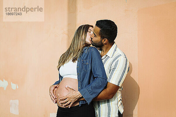 Schwangere Frau küsst Mann in der Nähe der Wand