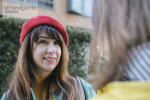 Glückliche Frau mit roter Baskenmütze im Gespräch mit einer Freundin