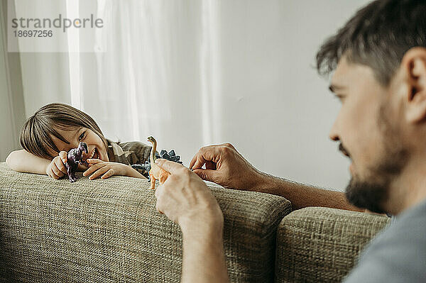 Vater und Sohn spielen zu Hause mit Spielzeugdinosauriern auf dem Sofa