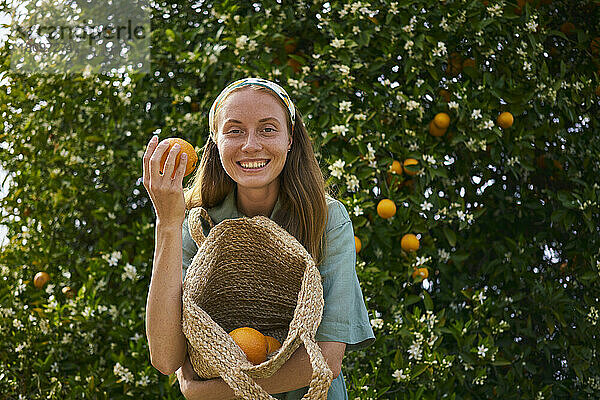Glückliche Frau hält einen Korb mit Bio-Orangen im Obstgarten