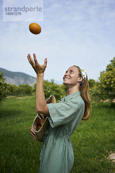 Lächelnde Frau wirft Orange im Obstgarten