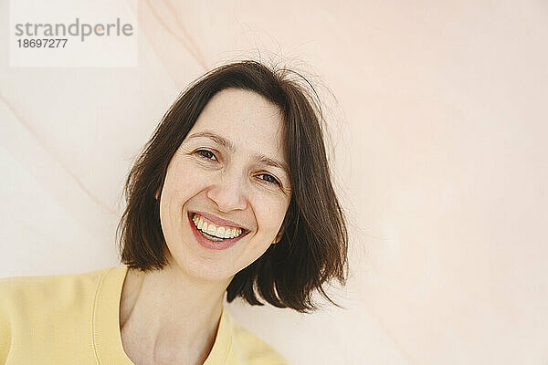 Lächelnde Frau mit kurzen braunen Haaren auf rosa Hintergrund