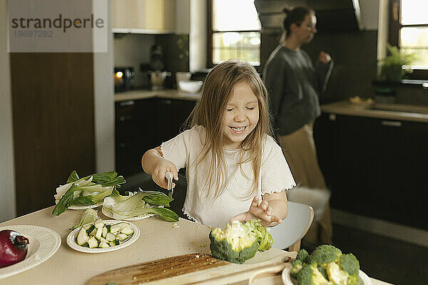 Fröhliches Mädchen schneidet Gemüse in der Küche