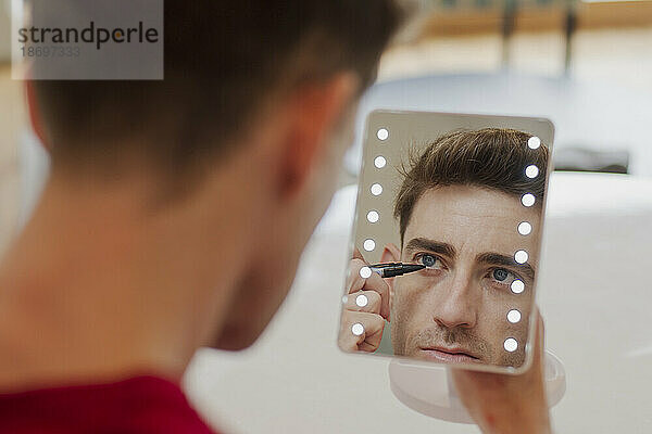 Mann trägt Make-up auf und schaut in den Spiegel