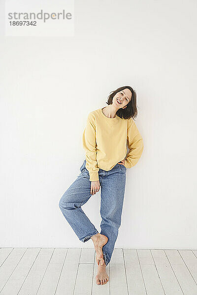 Smiling woman in casual clothes leaning on white wall