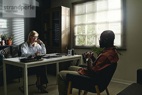 Patient sitzt auf Stuhl mit Psychologe neben Schreibtisch im Büro