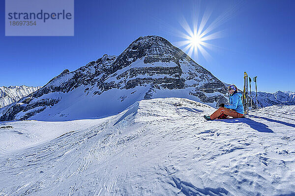 Österreich  Tirol  Sonne scheint über einer Skifahrerin  die am Torhelm eine Pause macht