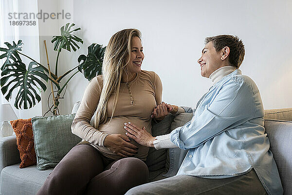 Ältere Frau mit schwangerer Tochter sitzt zu Hause auf dem Sofa