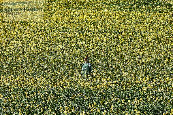 Frau steht inmitten gelber Rapsblüten im Feld