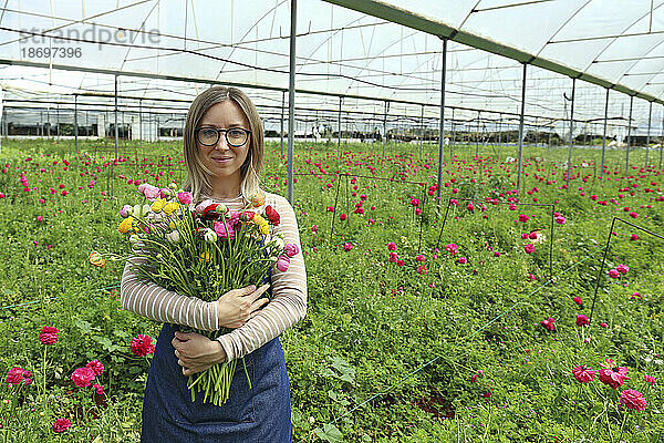 Lächelnder Bauer hält einen Blumenstrauß im Gewächshaus