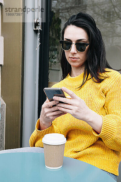 Junge Frau schreibt Textnachrichten per Smartphone im Straßencafé