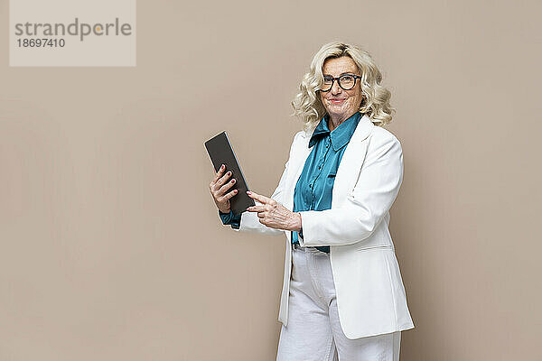 Ältere Geschäftsfrau hält Tablet-PC vor farbigem Hintergrund
