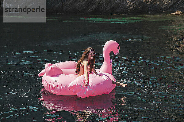 Fröhliches Teenager-Mädchen schwimmt im Urlaub auf einer Flamingo-Luftmatratze