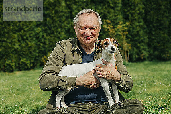 Älterer Mann hält Hund  der auf Gras im Hinterhof sitzt