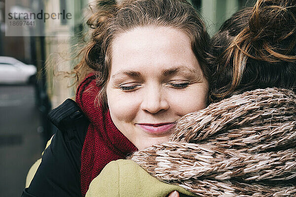 Lächelnde Frau mit geschlossenen Augen umarmt ihre Freundin