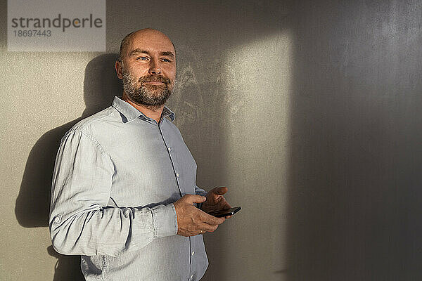 Reifer Geschäftsmann hält Mobiltelefon an einer Wand