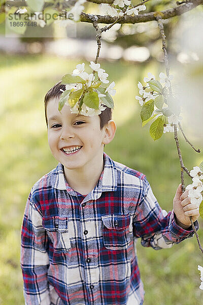 Lächelnder Junge hält im Frühling einen Ast im Hinterhof