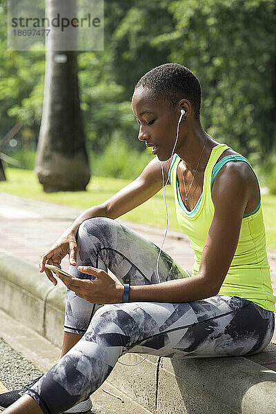 Frau surft mit Smartphone im Internet und sitzt auf Gehweg im Park
