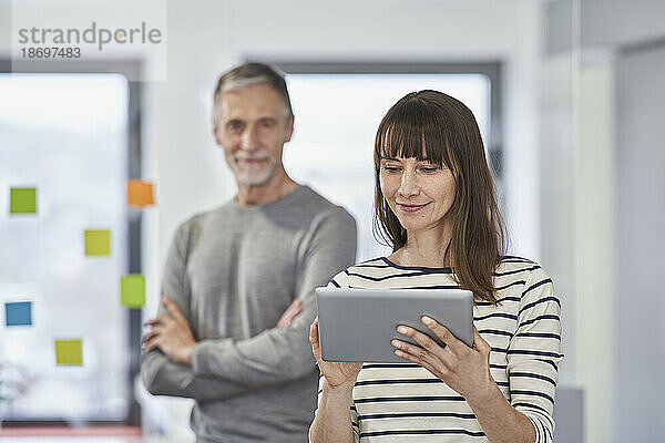 Geschäftsfrau nutzt Tablet-PC mit Kollege im Hintergrund im Büro