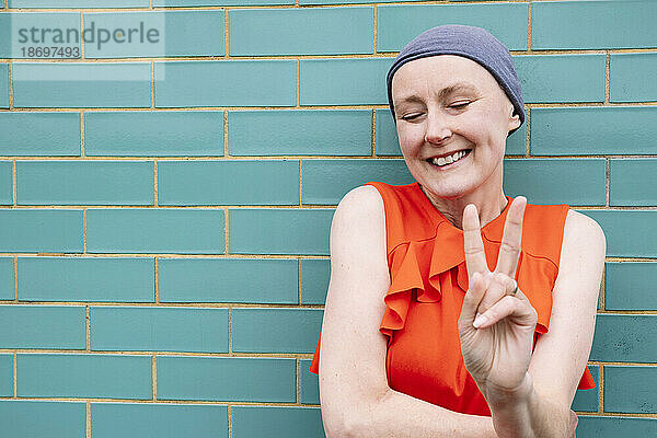Lächelnde Frau gestikuliert ein Friedenszeichen an einer Ziegelwand