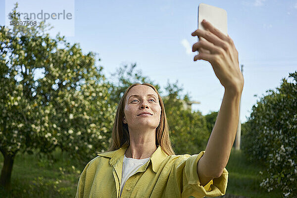 Frau macht Selfie mit Smartphone im Garten