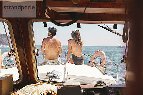 Mann und Frau sitzen auf dem Bug des Schiffes und werden durch die Windschutzscheibe gesehen
