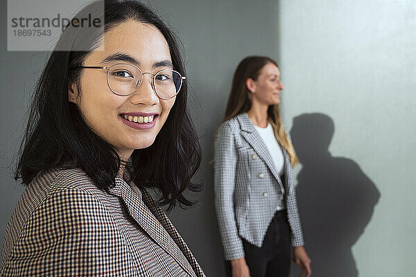 Porträt einer lächelnden Geschäftsfrau mit einem Kollegen im Hintergrund