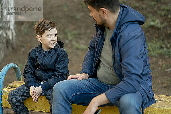 Sohn unterhält sich mit Vater  der auf einer Bank im Park sitzt