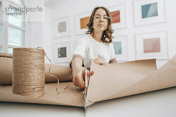 Fashion designer cutting wrapping paper by thread spool at workshop