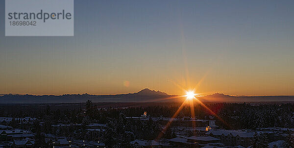 Sonnendurchbruch über Bergen und Stadtbild bei Sonnenuntergang; Surrey  British Columbia  Kanada