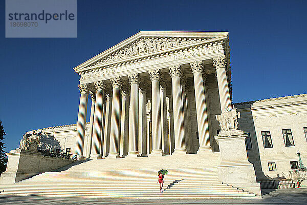 Frau mit Regenschirm in leuchtenden Farben geht die Stufen des Obersten Gerichtshofs der USA in Washington  DC  USA hinauf; Washington  District of Columbia  Vereinigte Staaten von Amerika
