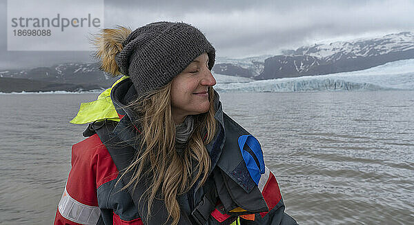 Nahaufnahme einer Frau mit blonden Haaren und Wollmütze  die eine Bootstour auf der Fjallsárlón-Gletscherlagune genießt; Südisland  Island