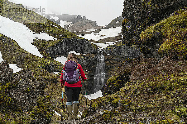 Nahaufnahme einer Frau von hinten  die steht und den Mulagljufur-Canyon  ein Paradies für Wanderer  überblickt  mit einem atemberaubenden Blick auf einen Wasserfall durch die moosbedeckten Klippen; Vik  Südisland  Island