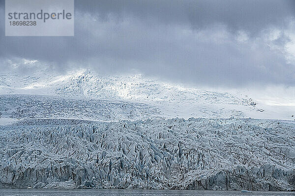 Der Blick auf das blaue Eis der Endstation des Fjallsjökull-Gletschers hebt sich von den grauen  nebligen Wolken ab  aufgenommen von der Fjallsarlon-Gletscherlagune am südlichen Ende des berühmten isländischen Gletschers Vatnajökull im Süden Islands; Südisland  Island