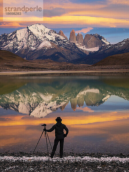 Blick von hinten auf die Silhouette eines Fotografen mit Kamerastativ  der bei Sonnenaufgang am Ufer des Lago Azul steht und Pumas verfolgt; Nationalpark Torres del Paine  Patagonien  Chile