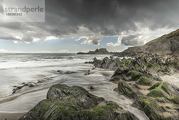 Langzeitbelichtung von Wellen  die am Strand von Long Strand entlangkommen  und der felsigen Küste des Atlantischen Ozeans unter einem bewölkten Himmel; Castlefreke  West Cork  Irland