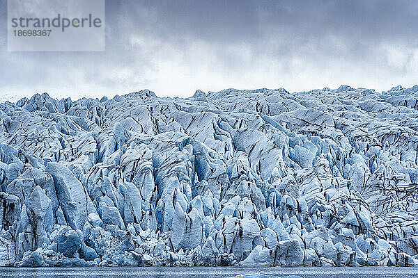 Nahaufnahmen der Fjallsarlon-Gletscherlagune auf die zerklüfteten blauen Eisformen des Endpunkts des Fjallsjökull-Gletschers  der sich von den grauen  nebligen Wolken abhebt  am südlichen Ende des berühmten isländischen Gletschers Vatnajökull im Süden Islands; Südisland  Island