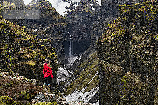 Frau steht und blickt auf den Mulagljufur-Canyon  ein Wanderparadies  mit atemberaubender Aussicht auf einen Wasserfall und die moosbedeckten Klippen; Vik  Südisland  Island
