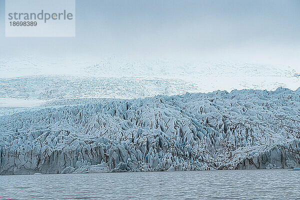 Der Blick auf das blaue Eis des Fjallsjökull-Gletschers sticht in der nebligen Atmosphäre von der Fjallsarlon-Gletscherlagune am südlichen Ende des berühmten isländischen Gletschers Vatnajökull im Süden Islands hervor. Südisland  Island