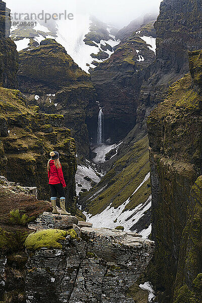 Frau steht und blickt auf den Mulagljufur-Canyon  ein Wanderparadies  mit atemberaubender Aussicht auf einen Wasserfall und die moosbedeckten Klippen; Vik  Südisland  Island