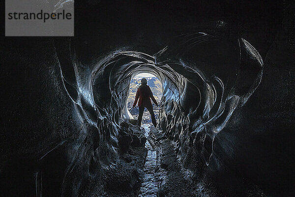 Blick durch eine Eishöhle auf eine Frau  die auf einer Reise in Island einen Gletscher erkundet; Vik  Südisland  Island